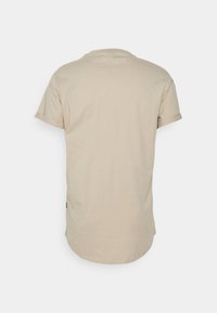 T-shirt beige à manches courtes vu de dos avec un ourlet arrondi et une couture simple sur un fond uni.