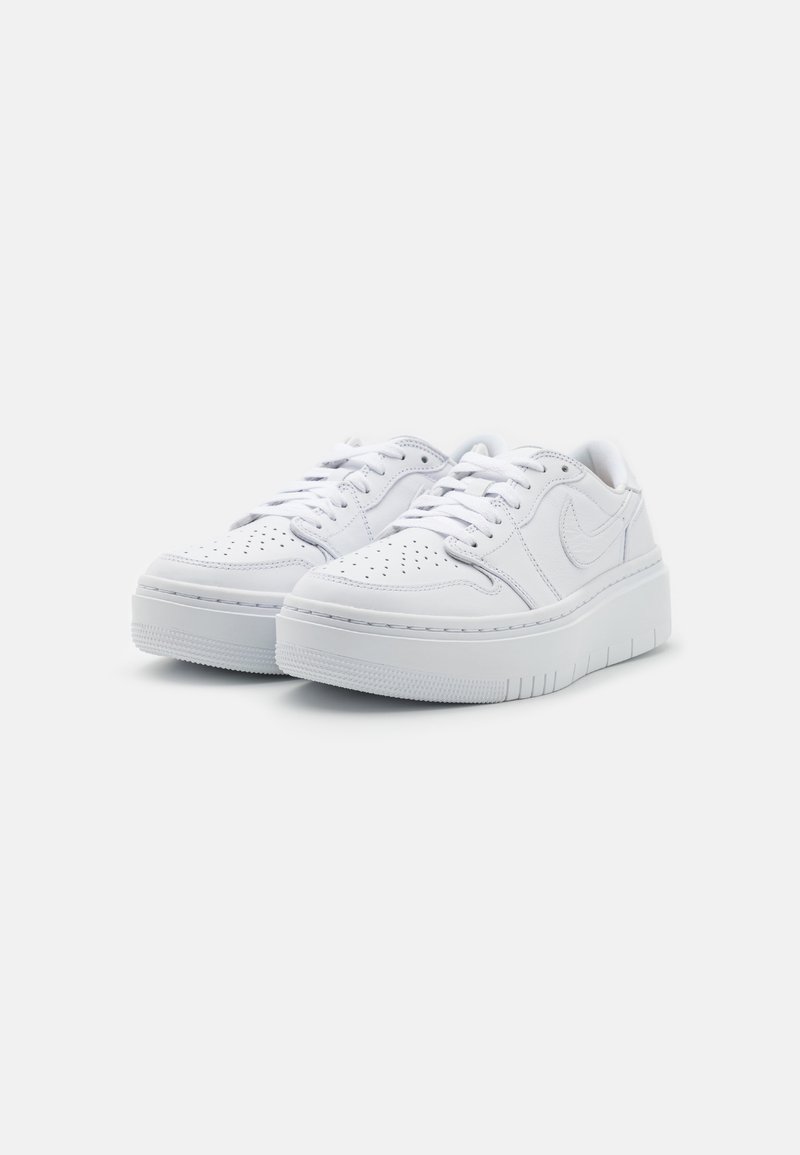 Baskets basses blanches avec un bout perforé, un design à lacets, une semelle rembourrée, une semelle extérieure en caoutchouc texturé et un branding minimaliste sur le côté.