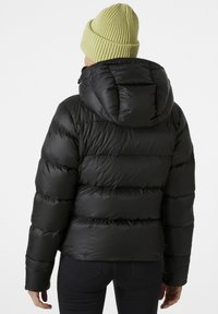 Schwarze Daunenjacke mit Kapuze, mit gesteppten Abschnitten, einer glatten Außentextur und einer Person, die eine hellgrüne Strickmütze trägt.