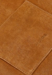 Tan suède portemonnee met een gladde textuur, reliëf logo detail en contrasterende stiksels. Compact rechthoekig ontwerp met een eenvoudige esthetiek.