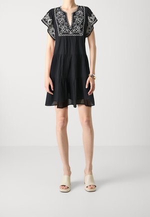 Black short dress with embroidered floral details in white. Features cap sleeves, a round neckline, and a flowing skirt. Worn with beige platform sandals.