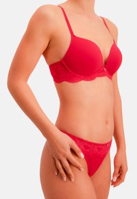 Rød blonde-bh og matchende undertøjssæt. Bh'en har formstøbte skåle med justerbare stropper, blondekant og dekorative metaldetaljer.
