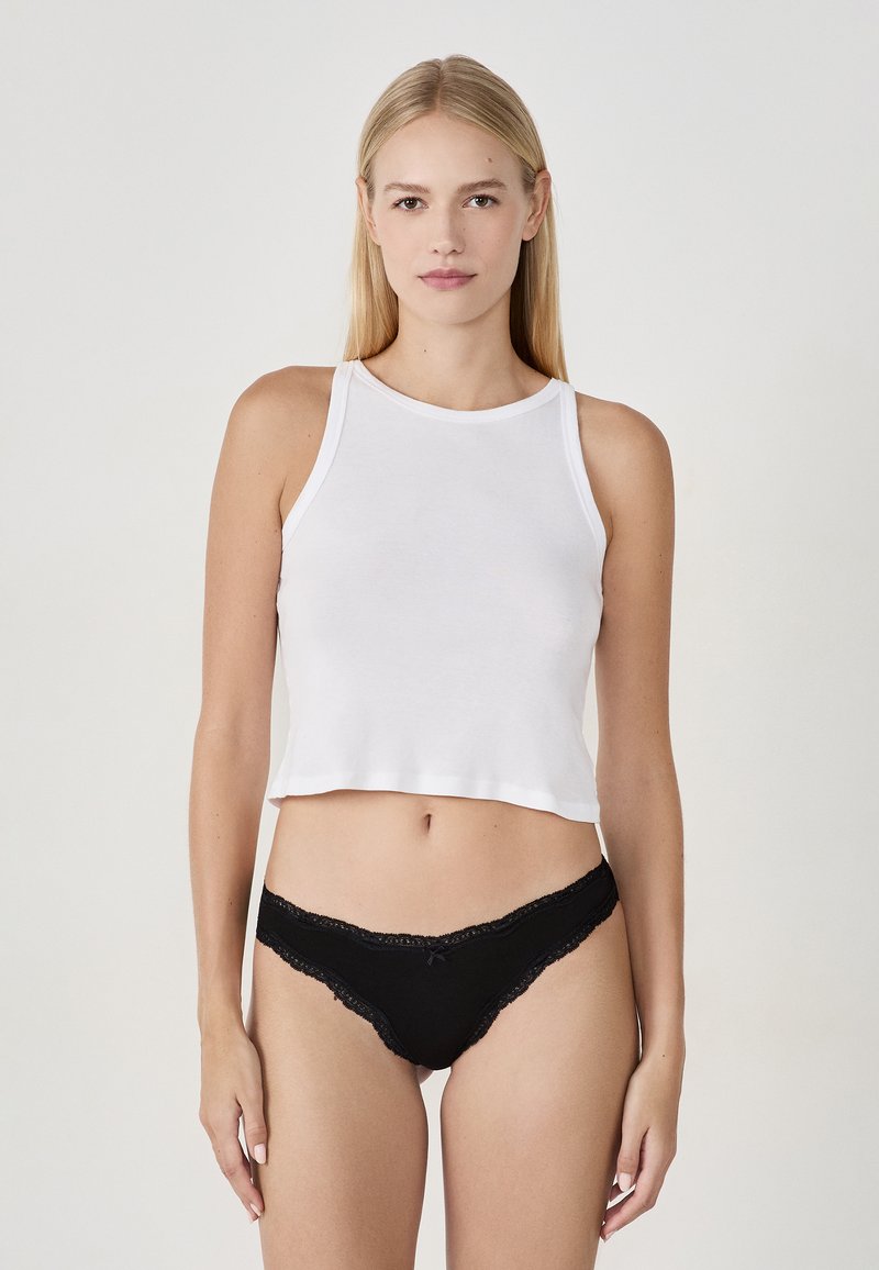 Haut court blanc en coton doux, associé à une culotte noire ornée de dentelle avec un petit nœud au centre devant.