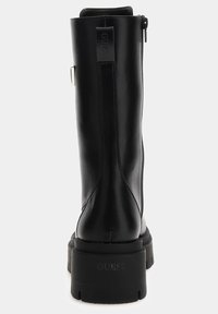 Botte noire en cuir montant jusqu'au genou avec une semelle épaisse, une fermeture éclair latérale et une étiquette de marque. Présente une texture lisse et un design minimaliste.