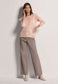 Hellrosa marmoriertes Sweater mit 3/4-Ärmeln, kombiniert mit taupefarbenen, weit geschnittenen Hosen und nudefarbenen Blockabsatzschuhen.