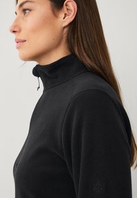Zwart fleece pullover met hoge kraag, voorzien van een rits en textuurstof. Opvallend detail: klein embleem op de linker mouw.