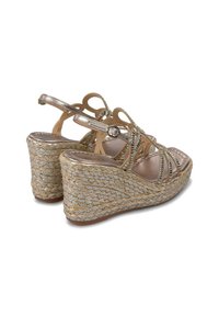 Sandali con zeppa caratterizzati da una fascia metallica dorata, texture intrecciata e una base in juta intrecciata. Stile con punta aperta e chiusura a fibbia.