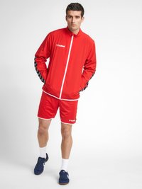 Rød træningsdragt med sorte og hvide mønstrede detaljer, der inkluderer en zip-up jakke og matchende shorts. Fremstillet af glat, letvægtsstof.