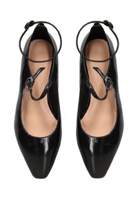 Zwarte gepatineerde leren flats met puntige neuzen, enkelriemen en zilveren gespen, met tan kleurige zolen op een witte achtergrond.