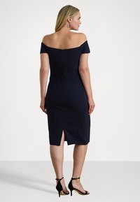 Tumši zila, bez plecu kleita ar piegulošu siluetu, līdz ceļgaliem, ar atvērta mugura. Valkā ar melniem augstiem papēžiem.