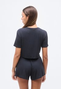 Μαύρο σετ από ριμπ ύφασμα δύο τεμαχίων που περιλαμβάνει ένα κοντό τοπ με κοντά μαν ίκια και σορτς με ψηλή μέση και άνετη εφαρμογή. Μαλακή υφή, μινιμαλιστικός σχεδιασμός.