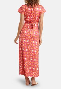 Maxikleid aus glänzendem roten Stoff mit kreisförmigen und floralen Mustern in Orange und Creme. Schnürrung im Rücken, kurze Ärmel und knöchellang.
