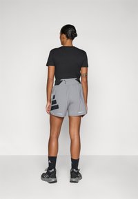 Svart kortermet skjorte kombinert med grå treningsshorts med svarte detaljer og en glidelåslomme bak, iført svarte sokker og joggesko.