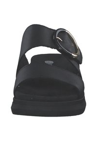 Sandale noire avec une large sangle sur le pied et un accent métallique circulaire. Semelle intérieure rembourrée en douceur et semelle basse texturée.