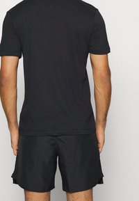 Camiseta negra de manga corta con cuello redondo; combinada con pantalones cortos deportivos negros con un diseño de abertura lateral, fabricados con un tejido suave y ligero.