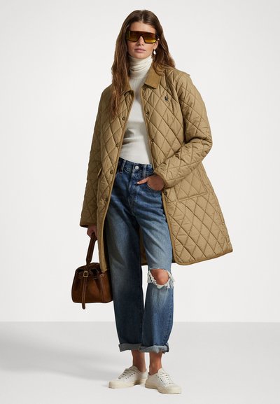 Manteau en khaki matelassé, pull col roulé, jeans en denim déchirés, baskets blanches et sac à main marron. Le modèle porte des lunettes de soleil teintées jaune.