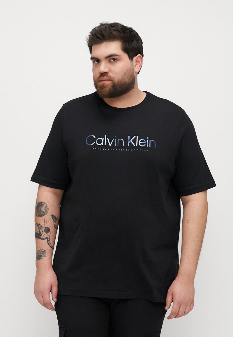 Svart bomulls t-skjorte med kort erm som har en blå og hvit "Calvin Klein" logo på fronten, med en avslappet passform og rund hals.