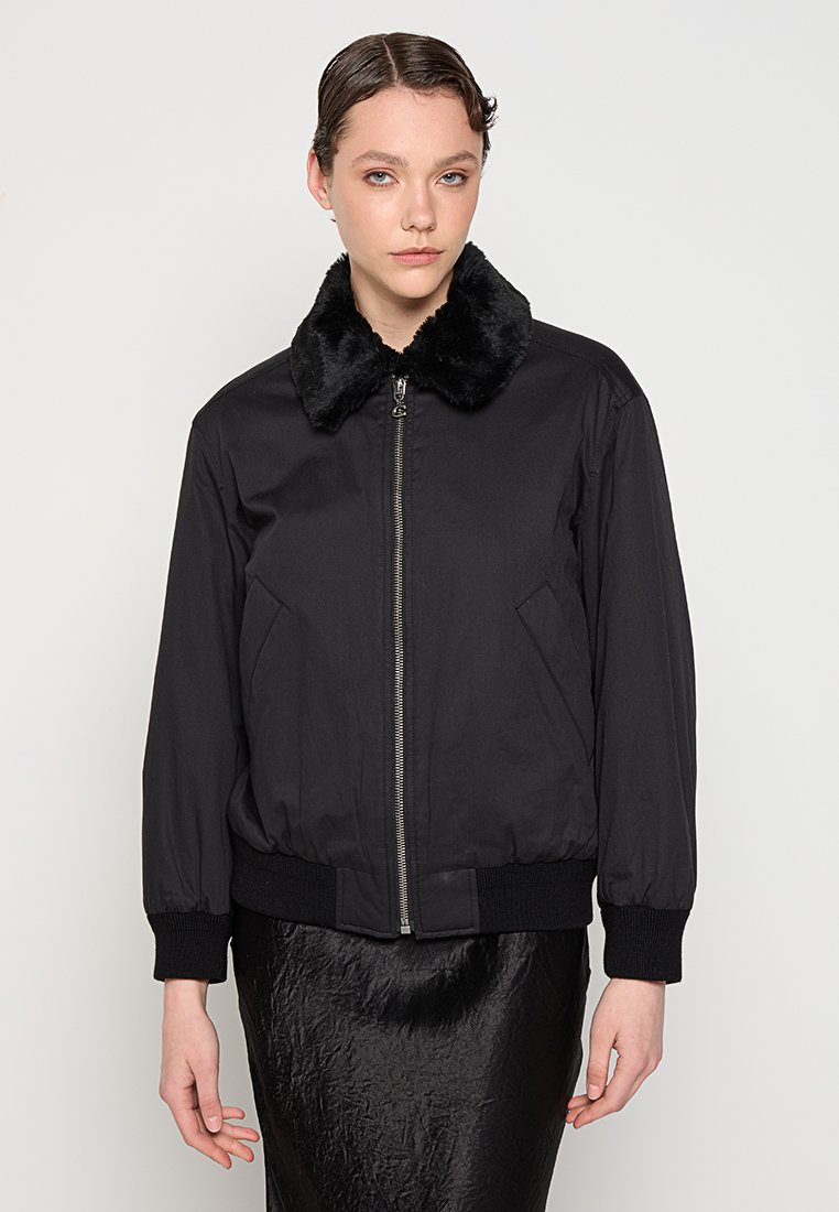 Czarna kurtka bomber z kołnierzem z sztucznego futra, z zamkiem z przodu, kieszeniami po bokach i prążkowanymi mankietami. Gładki materiał i wyraźny kształt.