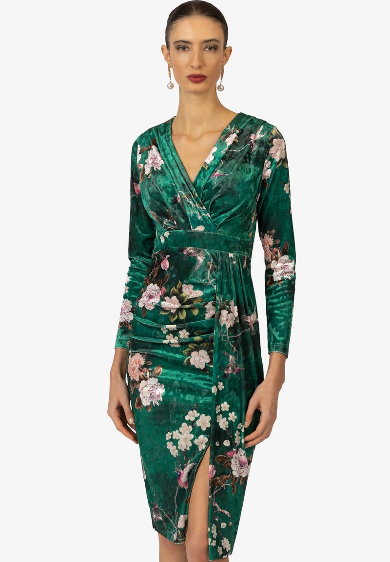 Abito verde in velluto con stampa floreale, design avvolgente, maniche lunghe e uno spacco frontale. Presenta una texture liscia e colori vivaci.
