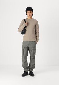 Beige knit sweater, gray cargo pants with multiple pockets, black bag, and black footwear. Simple design, textured knit, and functional cargo style.
