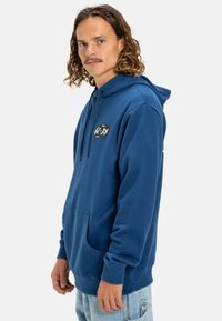 Blue hooded sweatshirt with a kangaroo pocket, made of fleece material, featuring a circular logo on the chest and drawstring for adjustment.