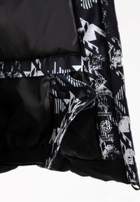 Schwarze Jacke mit gemustertem Innenfutter, das weiße geometrische Designs aufweist. Enthält wasserdichte, atmungsaktive Etiketten und ein Etikett aus recyceltem Material.