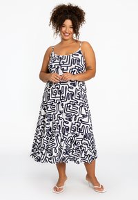 Weißes Kleid mit navyblauen abstrakten geometrischen Mustern, Spaghettiträgern, ausgestelltem Saum und einem Rüschensaum. Das Material wirkt leicht und glatt.