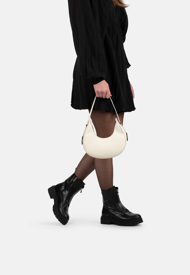 Bolso de cuero blanco en forma de media luna, con un asa corta. Combinado con un vestido negro y unos botines negros de textura.
