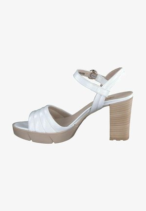Weiße Sandalen mit Absatz, die einen breiten, strukturierten Riemen über den Zehen, einen verstellbaren Knöchelriemen und einen klobigen, beige gerippten Absatz haben.