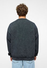 Donkergrijze sweatshirt met een ronde hals, verlaagde schouders en geribbelde boorden, gecombineerd met lichtblauwe jeans. Zachte textuur, minimalistisch ontwerp.