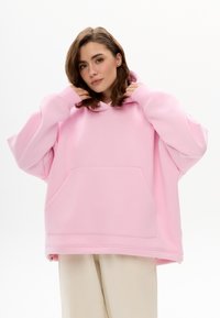 Übergroßer rosa Hoodie mit Kängurutasche, Kordelzugkapuze und gerippten Bündchen. Glatte Textur und lockere Passform.