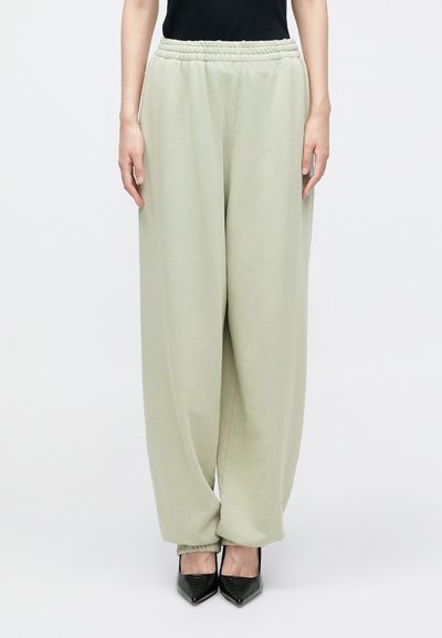 Light green sweatpants with an elastic waistband and tapered cuffs, made from soft material, paired with black pointed-toe shoes.