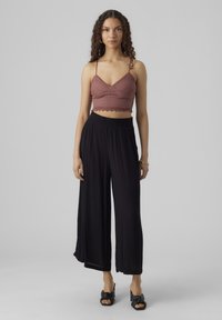 Burgundi csipke crop top, fodros szélekkel, széles lábú fekete nadrággal párosítva, laza fazonnal és puha textúrával. Fekete lábbeli.