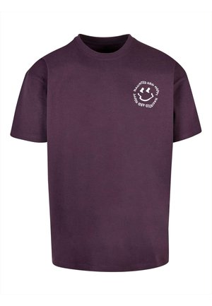 T-shirt di cotone viola con maniche corte, scollo rotondo e testo stampato bianco con design di faccina sorridente nell'area sinistra del petto.