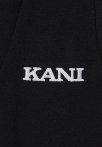 Crni materijal s bijelim izveznim tekstom koji ispisuje "KANI". Tekstura izgleda glatko, s blagim sjajem na svjetlosti.