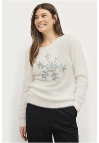 Weißer, flauschiger Pullover mit einem Pailletten-Schneeflocken-Design in Silber und Blau, mit Rundhalsausschnitt und langen Ärmeln, kombiniert mit schwarzen Hosen.