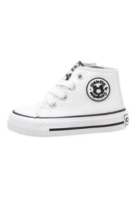 Zapatilla alta de lona blanca con suela de goma negra, puntera redonda, dos ojales blancos y parche circular con logo en el lado exterior.