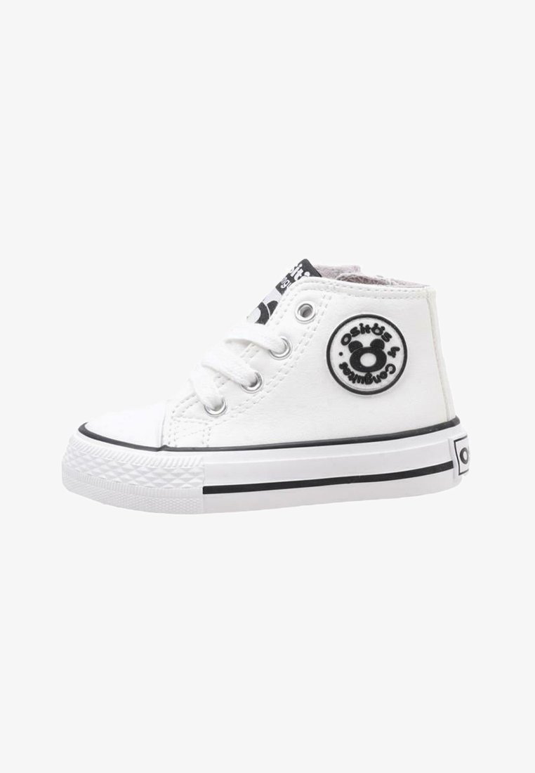 Zapatilla alta de lona blanca con suela de goma negra, puntera redonda, dos ojales blancos y parche circular con logo en el lado exterior.