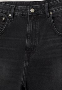 Black denim jeans front view showing button closure, belt loops, and front pockets with metal rivets.