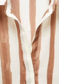 Gros plan d'un tissu avec des rayures verticales marron et blanc cassé présentant un col ou un décolleté partiellement ouvert.