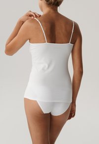 Biała bawełniana kamizelka z regulowanymi cienkimi ramiączkami i dopasowanym krojem, w połączeniu z białą bielizną. Gładka tekstura i minimalistyczny wzór.