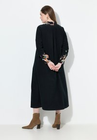 Abito in corduroy nero con maniche a tre quarti, polsini con motivo e piega sul retro. Paio di stivaletti alla caviglia in suede beige con tacco impilato.