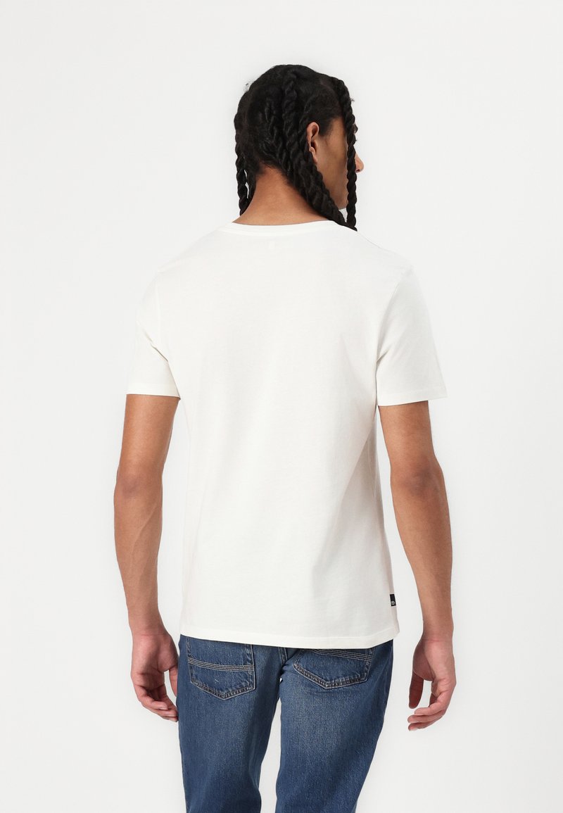 Off-white T-shirt met korte mouwen, ronde halslijn, zachte katoenstof, normale pasvorm, gecombineerd met blauwe denim jeans, minimale zichtbare branding.