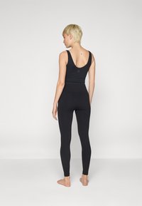 Fekete bordázott leggings, magas derékkal, egy megfelelő ujjatlan toppal párosítva. Puha anyag, sima textúrával. Nincs észlelhető minta.