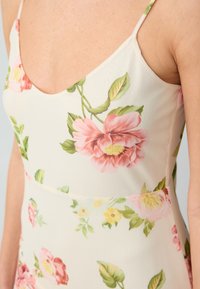 Robe florale avec un fond crème, des bretelles fines et une coupe ajustée. Décorée de motifs de fleurs roses, jaunes et vertes.
