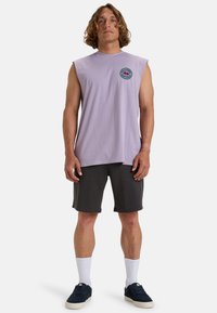 Paarse mouwloze t-shirt, van katoen, met een ronde afbeelding op de borst. Gecombineerd met donkere shorts, witte kousen en marineblauwe schoenen.
