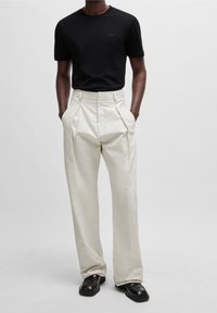 Černé vypasované tričko s nenápadným logem, spárované s vysokými krémovými rozšířenými kalhotami a černými koženými botami.