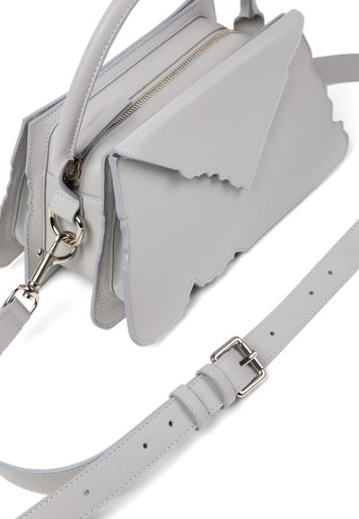 Sac bandoulière en cuir gris clair avec rabat aux bords festonnés, fermeture éclair argentée, et sangle ajustable avec boucle argentée sur fond blanc.