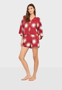 Ensemble rouge deux pièces comprenant un haut à manches courtes avec motif étoilé blanc et un short assorti. Tissu doux et léger avec une coupe décontractée.