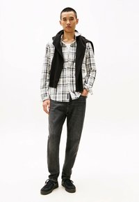 Plaid button-up shirt in white and black, layered with a black sweater. Worn with dark jeans and black sneakers, showcasing a classic casual look.